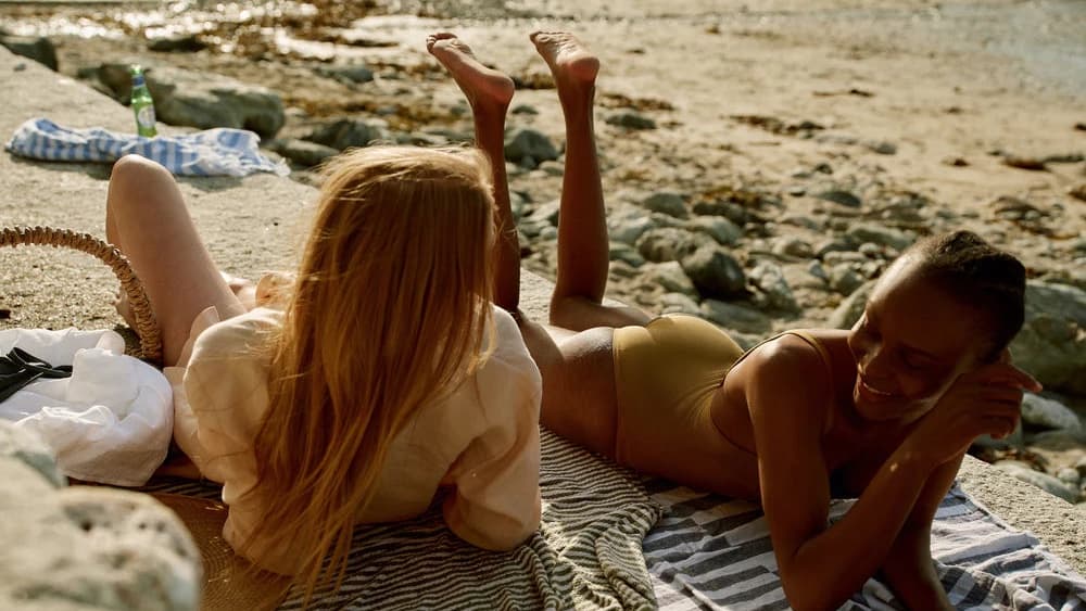 Two women in Asceno swimwear and linen relaxing on a rocky beach